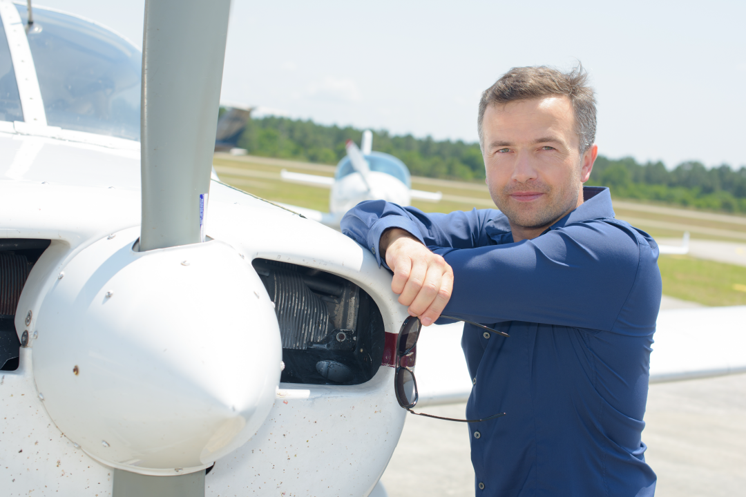adult male smiling and leaning against single engine aircraft holding sunglasses