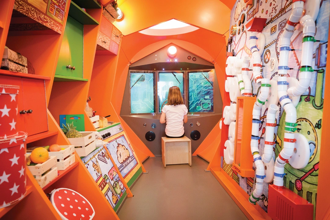 girl pretending to steer large ship in a wildly decorated and very interactive playroom