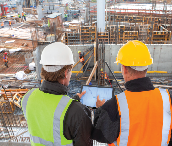 two construction engineers in safety gear looking over plans at worksite