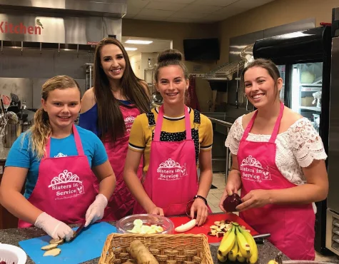 group of four young adult females all wearing matching aprons working to prepare a meal