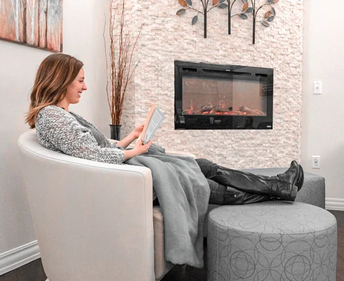 adult female sitting in comfy chair next to fireplace